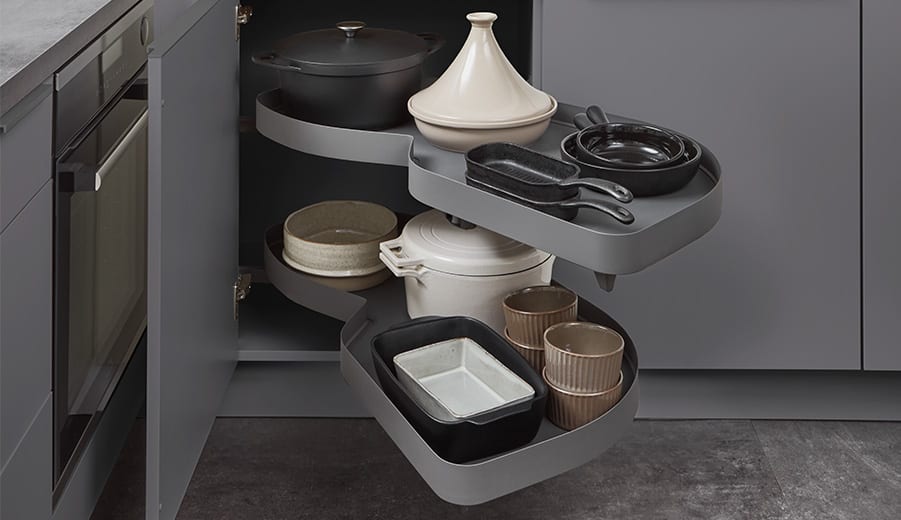Armoire d’angle ouverte, deux plateaux pivotants sortis du meuble, chargés de cocottes, plats et bols