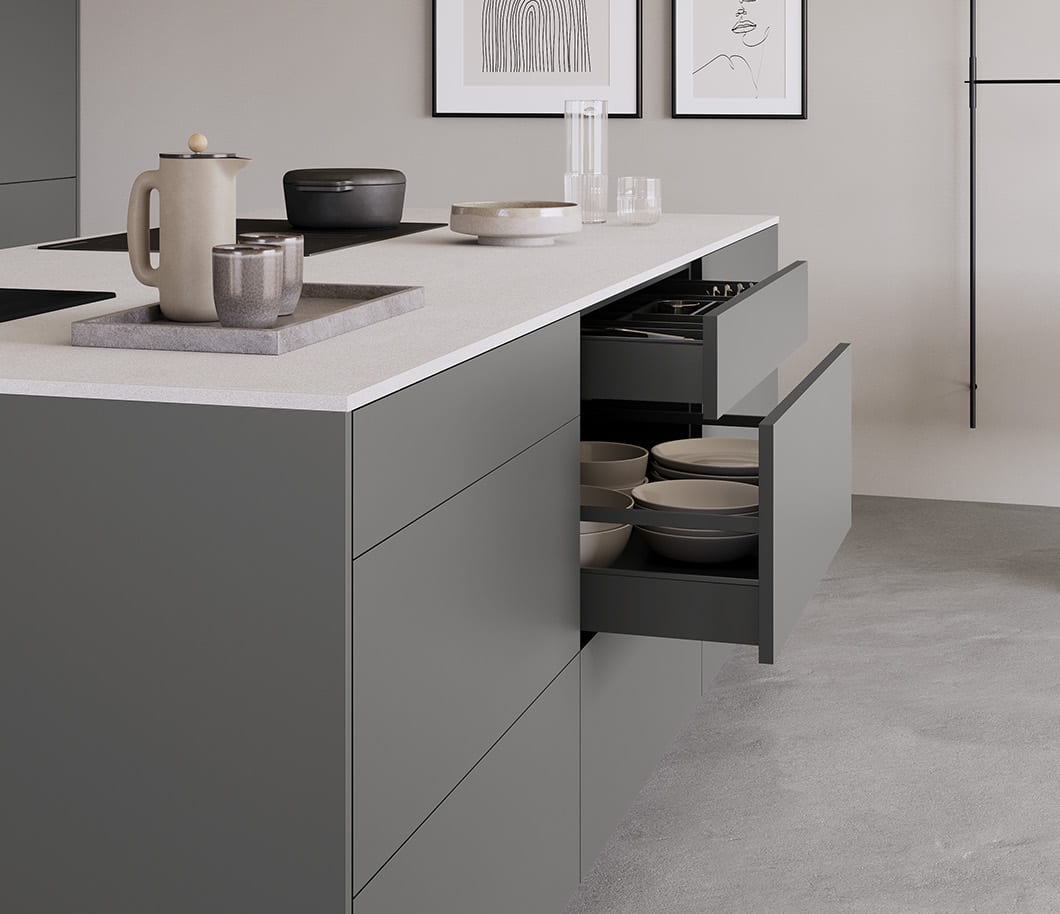 Îlot de cuisine gris à façades lisses : deux tiroirs sont sortis, l’un garni d’un range-couverts, l’autre de bols et d’assiettes debout