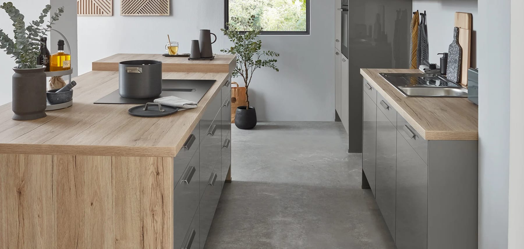 Cuisine à deux plans parallèles : caissons gris mats, plan de travail et joue d’îlot en décor chêne clair descendant jusqu’au sol