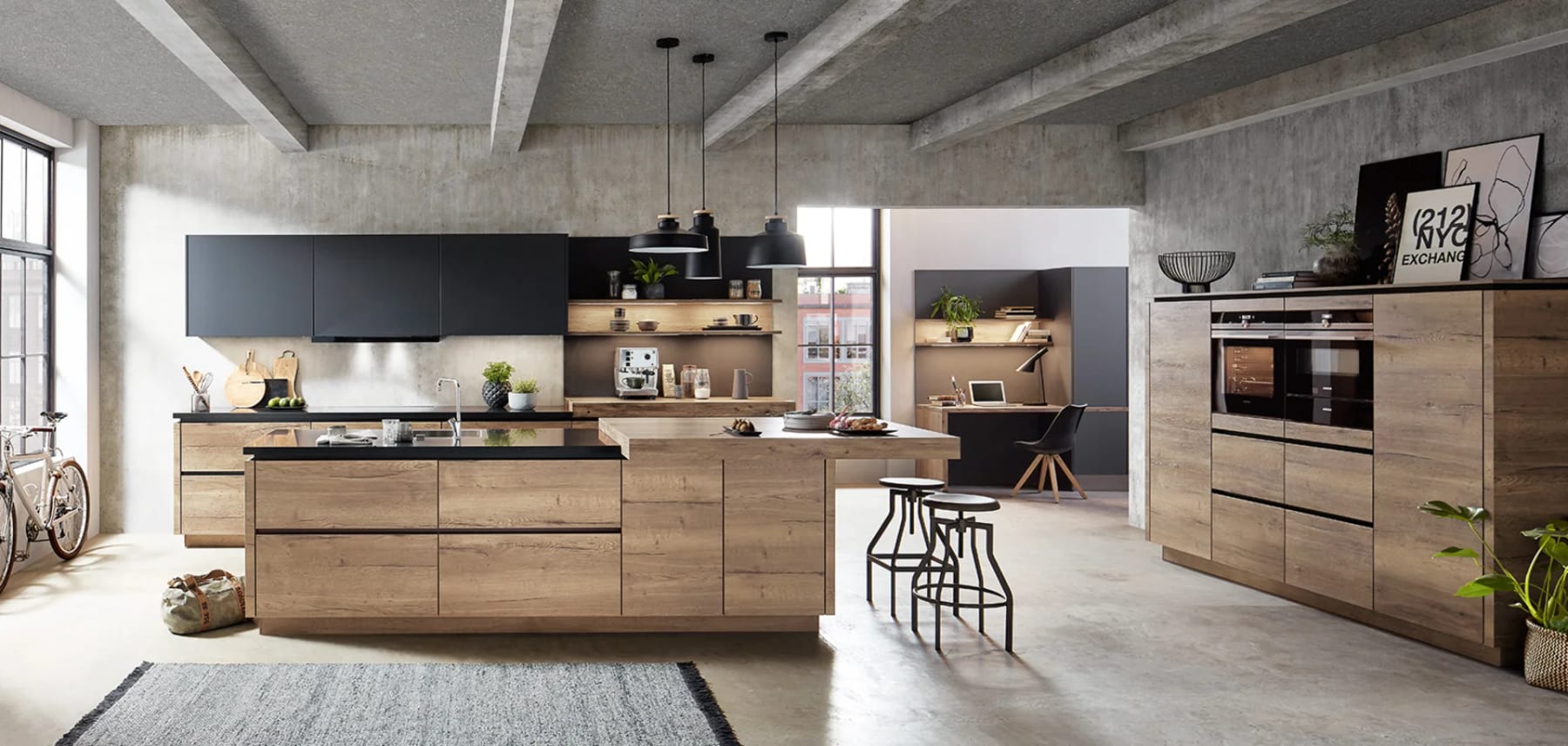 Cuisine en décor chêne sous un plafond de béton brut, îlot avec assise, coin bureau aménagé au fond de la pièce