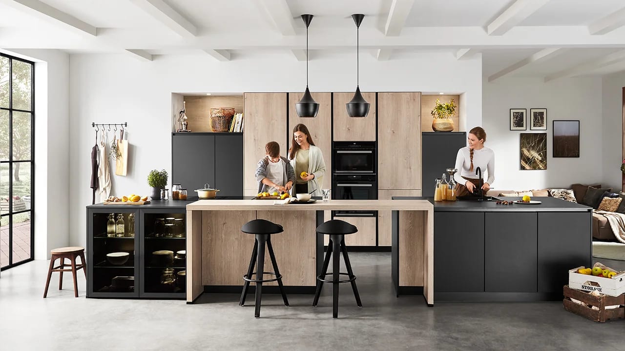Cuisine en décor chêne clair associée à des meubles noirs mats, îlot avec table haute intégrée