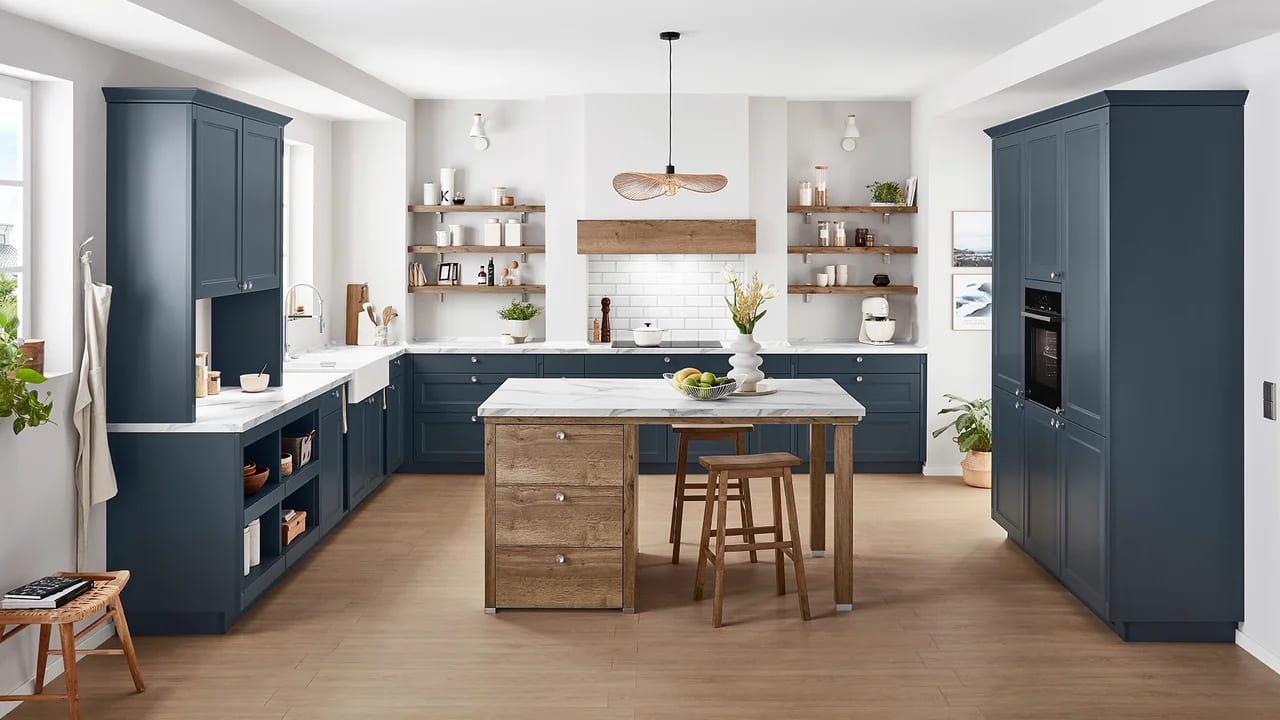 Cuisine à façades à cadre bleu canard, plan de travail effet marbre blanc, îlot en bois et crédence en carrelage blanc