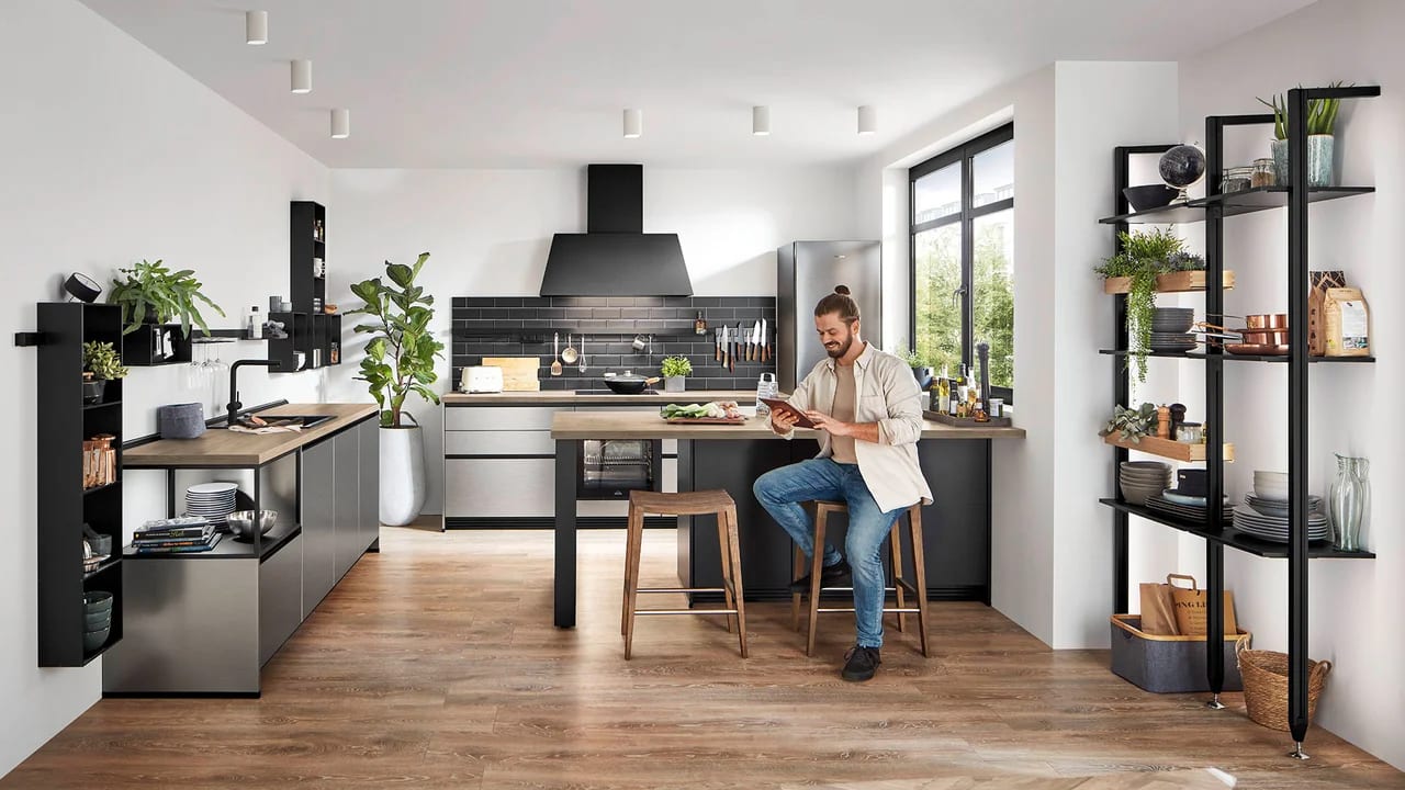 Cuisine en décor acier brossé, crédence en carrelage métro noir, plan de travail bois et étagères métalliques