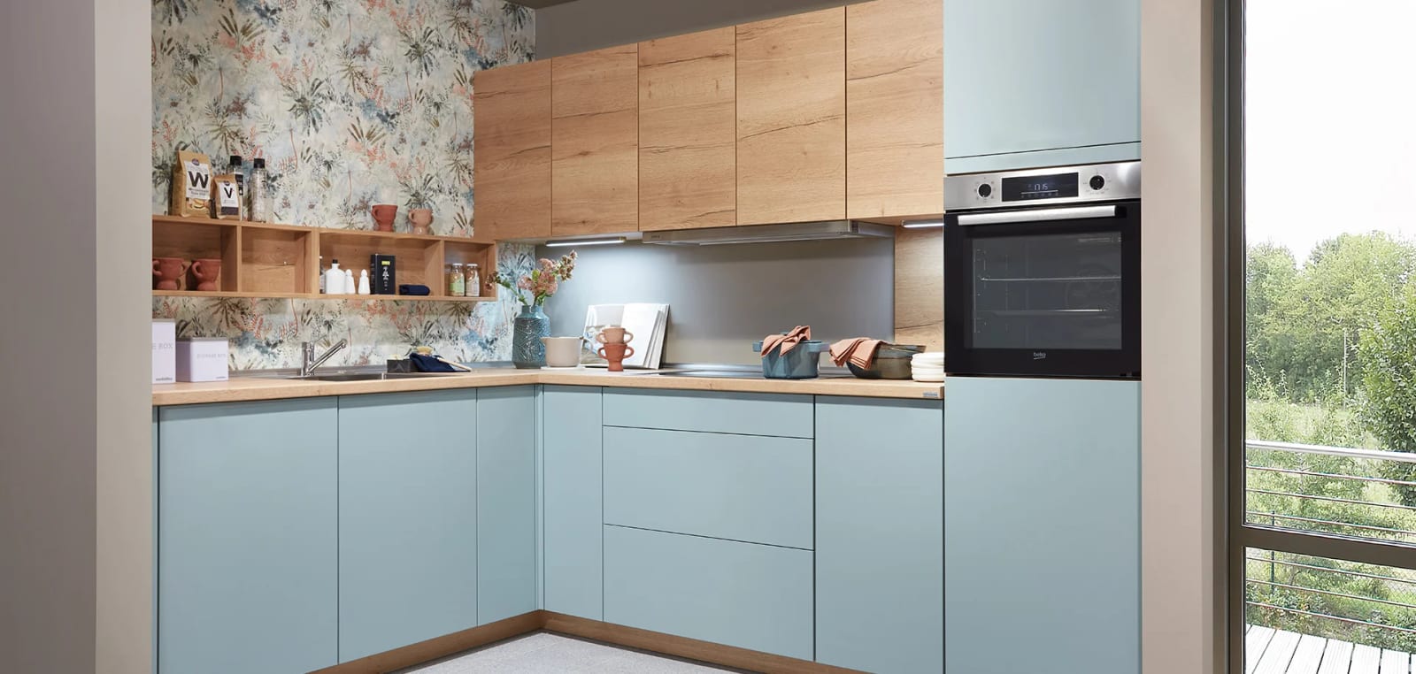 Cuisine en L, façades super-mates bleu aqua et meubles hauts en décor chêne, ouverte sur un balcon boisé