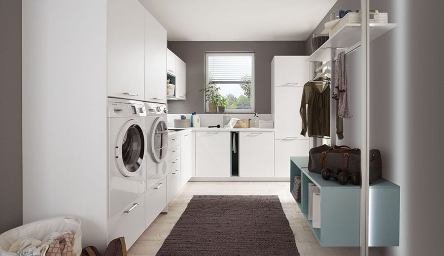 Buanderie blanche en L : lave-linge et sèche-linge superposés en colonne, plan de pliage sous la fenêtre, penderie de séchage et banc de rangement bleu clair
