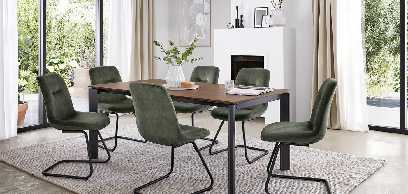 Salle à manger ouverte sur le jardin : table en bois massif à piétement noir, six chaises en velours vert, cheminée blanche et grandes baies vitrées