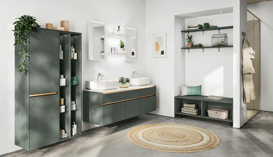 Salle de bains vert profond : colonne de rangement à étagères ouvertes, meuble double vasque suspendu à poignées dorées, miroir éclairé et banc à linge devant la douche