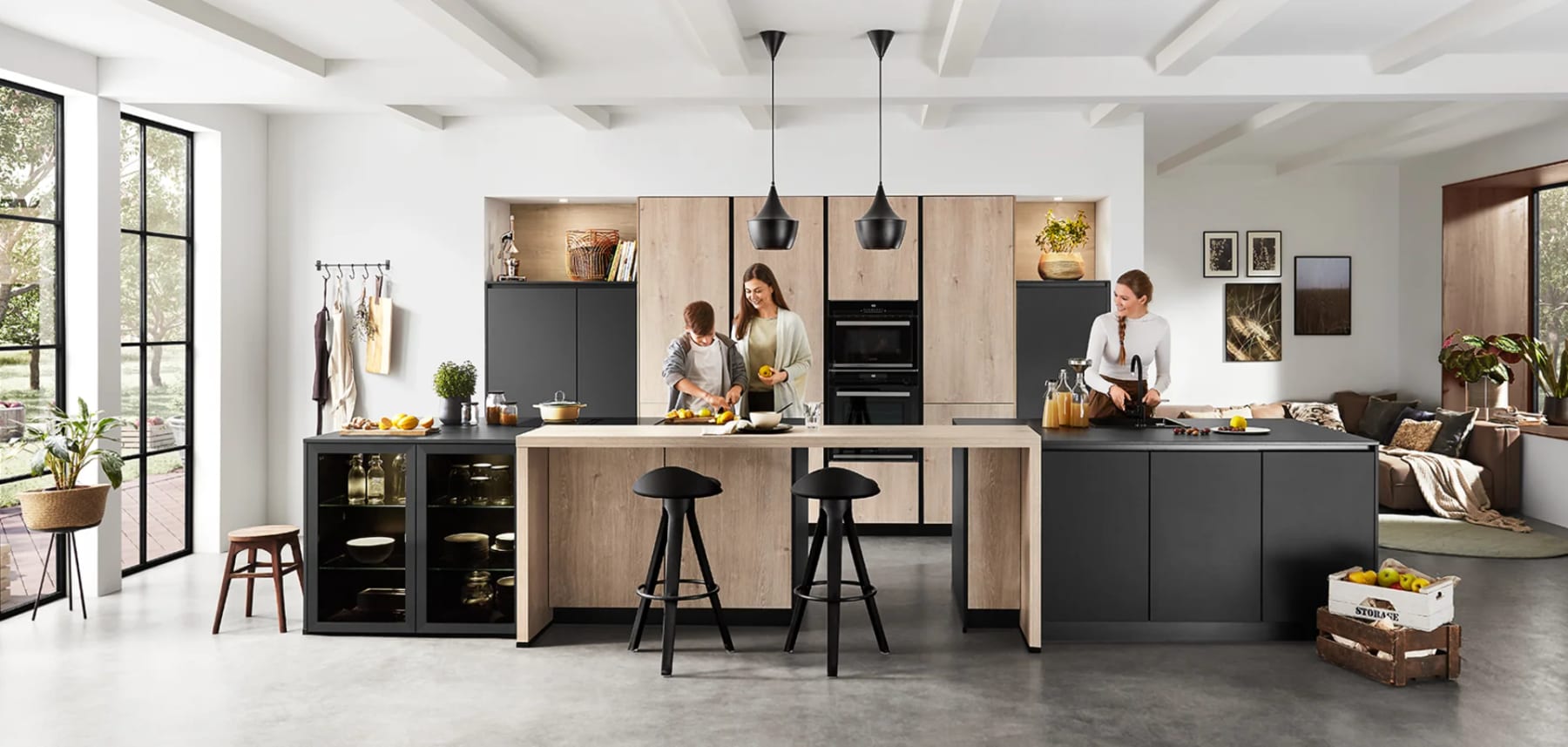 Trois personnes qui cuisinent ensemble autour d’un îlot, façades anthracite et décor de chêne, verrière au fond