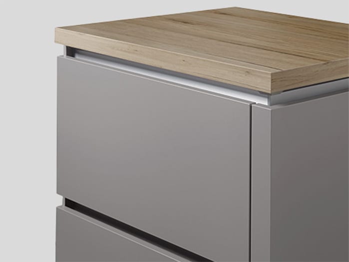 Meuble bas gris à deux tiroirs, gorge intégrée couleur inox courant entre les deux façades sous un plan de travail en bois