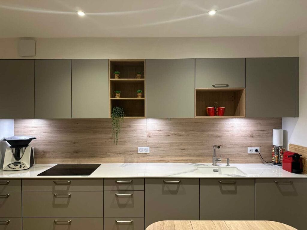 Cuisine linéaire posée par OXIA : façades gris kaki, crédence bois et plan clair