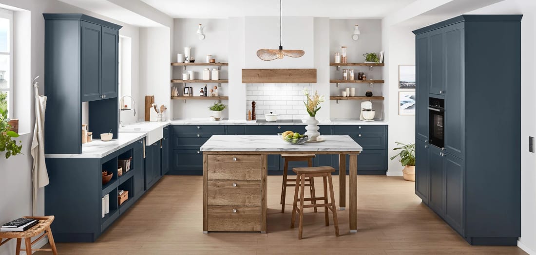Cuisine de campagne en L à façades à cadre bleu, évier de céramique sous fenêtre et table d’appoint en bois au centre