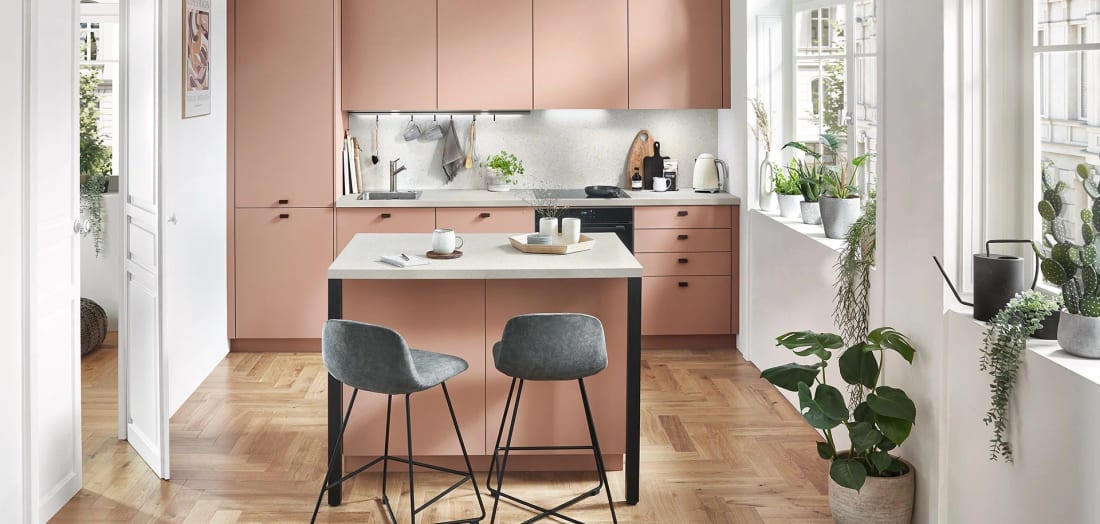 Cuisine corail mate dans un appartement ancien, meubles hauts sous plafond et petit îlot-comptoir pour deux