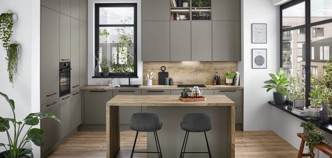 Petite cuisine gris taupe montée jusqu’au plafond, table-îlot en décor chêne et deux tabourets